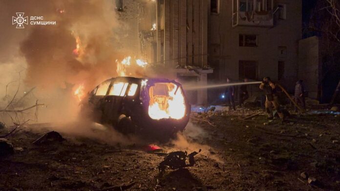 photo_2025-12-08_07-12-36 Rescuers extinguish a fire near a burning car and a destroyed high-rise building