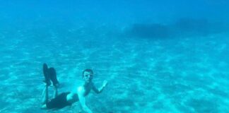 A swimmer underwater next to a large statue of Skidvard on the seabed.