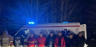 Затримані чоловіки біля автомобіля швидкої допомоги на кордоні