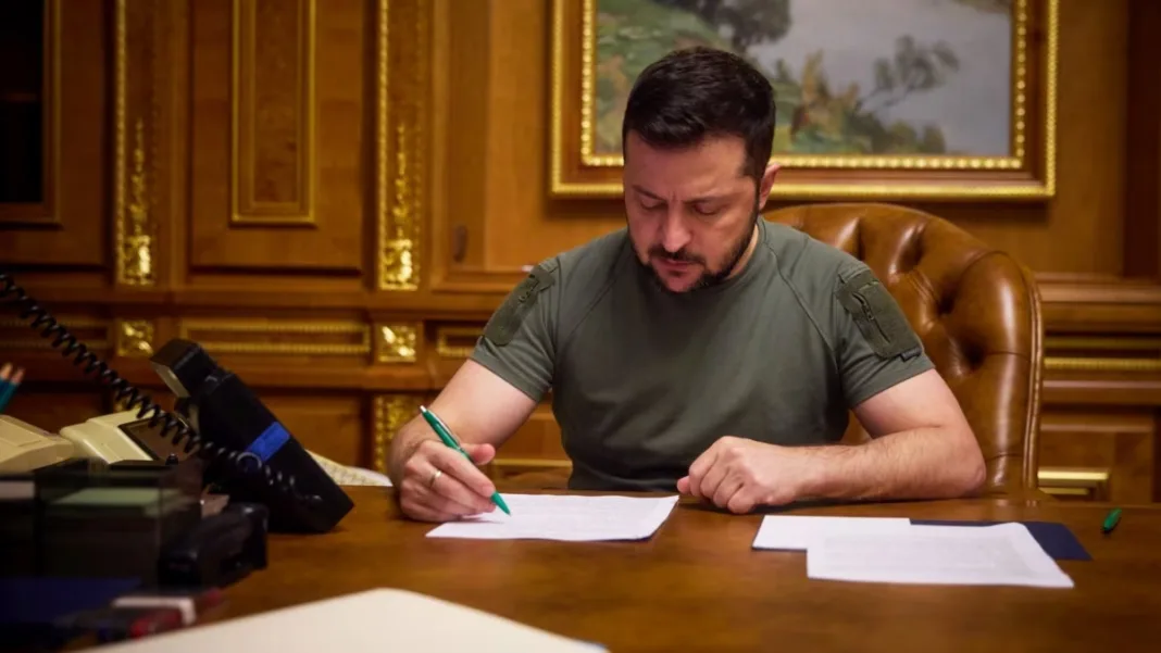 Володимир Зеленський підписує документи за робочим столом.