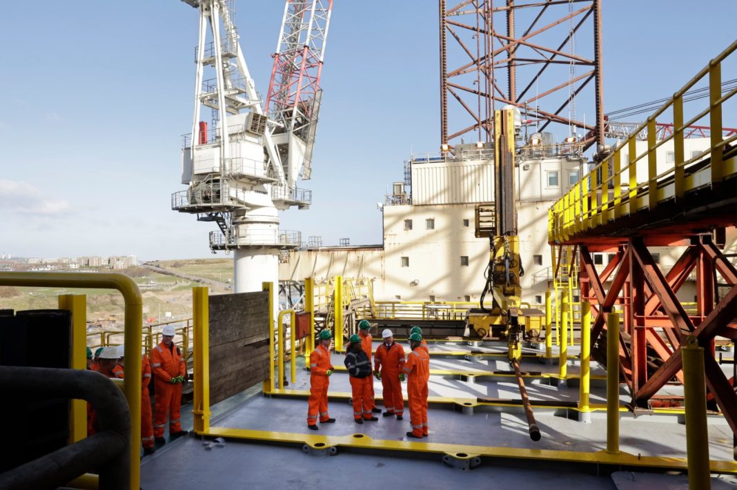 The photo shows a drilling platform in the North Sea against a cloudy sky.