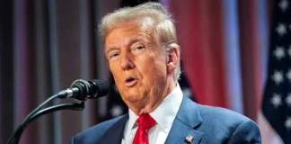 Donald Trump during a press conference, with the US flag in the background