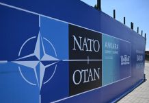 The NATO logo against a backdrop of military equipment