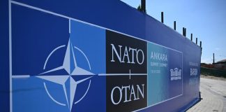 The NATO logo against a backdrop of military equipment