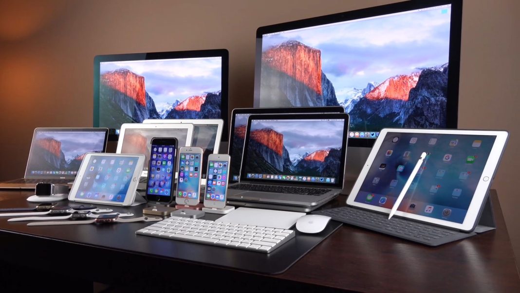obzor-sovremennyh-lineek-produkcii-apple Лінійка пристроїв Apple, включно з iPhone, iPad, MacBook, iMac та іншою технікою компанії, представленою на одному робочому столі.