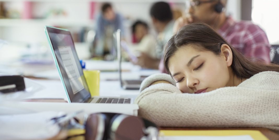 A young girl sleeps on her desk next to her laptop because of chronic fatigue and insomnia.