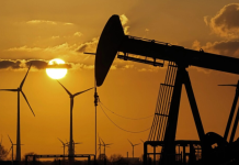 Oil prices have risen to a one-month high due to the escalation in the Strait of Hormuz An oil pumping station against a backdrop of wind farms at sunset