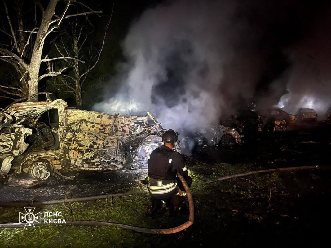 A State Emergency Service firefighter is putting out a fire amongst wrecked cars following a missile attack on Kyiv on the night of 14 July 2026.