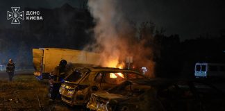 Rescue workers stand beside burning and damaged cars following the night-time attack on Kyiv.