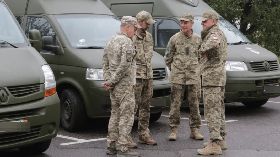 Четверо військових у камуфляжі розмовляють біля зелених службових мікроавтобусів Четверо військових у камуфляжі розмовляють біля зелених службових мікроавтобусів