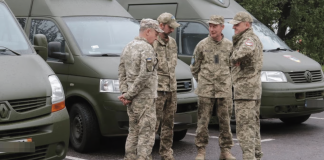 Four soldiers in camouflage are talking next to green service minibuses