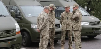 Четверо військових у камуфляжі розмовляють біля зелених службових мікроавтобусів
