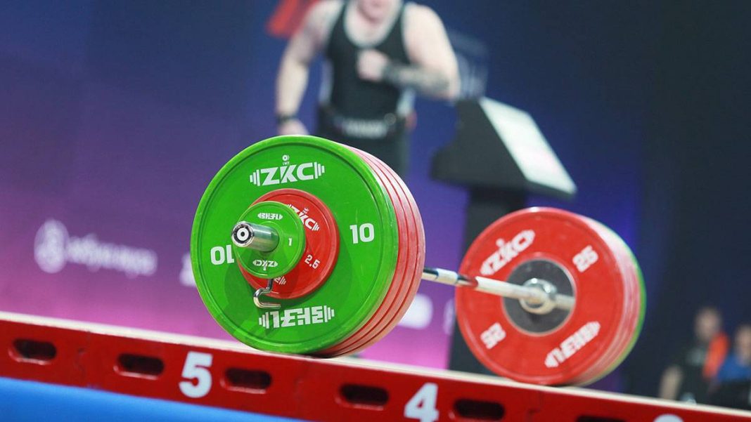 1200_6989b84382682c6e05a465a2 A barbell with coloured discs on the platform during an international weightlifting competition