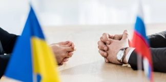 Ukraine wants to speed up negotiations with Russia and involve the EU Representatives from Ukraine and Russia are seated at the negotiating table, with the Ukrainian and Russian flags in the foreground