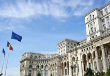 У Румунії після шести місяців кризи затвердили новий уряд Будівля Палацу парламенту Румунії в Бухаресті з прапорами Румунії та Європейського Союзу перед головним фасадом.