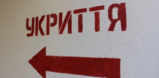 A red sign reading «SHELTER» with an arrow on a white wall