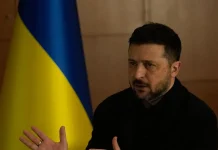 Президент України Володимир Зеленський у чорному одязі під час виступу на тлі державного прапора України.