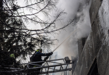 Rescue workers from the State Emergency Service are putting out a fire in a damaged building using a fire hose from a ladder truck.