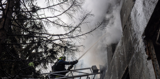 Rescue workers from the State Emergency Service are putting out a fire in a damaged building using a fire hose from a ladder truck.