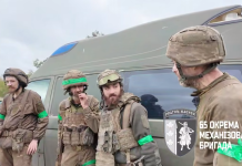 Four soldiers in full kit are standing next to an evacuation minibus
