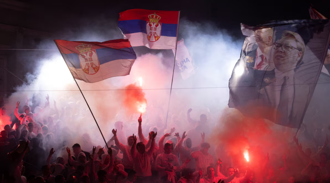 A crowd waving Serbian flags and holding lit flares