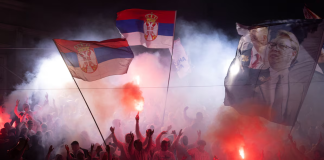 A crowd waving Serbian flags and holding lit flares