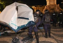 Поліція демонтувала 171 намет протестувальників у Португалії Поліцейські в захисному спорядженні несуть білий туристичний намет нічною площею.