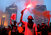Participants in an anti-government protest in Jakarta hold up red signal flares against the backdrop of the city’s skyscrapers during a demonstration against the policies of the Indonesian president