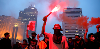 Participants in an anti-government protest in Jakarta hold up red signal flares against the backdrop of the city’s skyscrapers during a demonstration against the policies of the Indonesian president