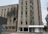 Пошкоджена багатоповерхова будівля з вибитими вікнами, слідами пожежі та зруйнованою частиною фасаду.