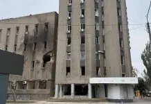 Пошкоджена багатоповерхова будівля з вибитими вікнами, слідами пожежі та зруйнованою частиною фасаду.