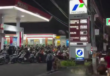 A queue of motorbikes and people outside the Pertamina petrol station at night
