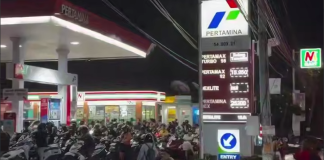 A queue of motorbikes and people outside the Pertamina petrol station at night