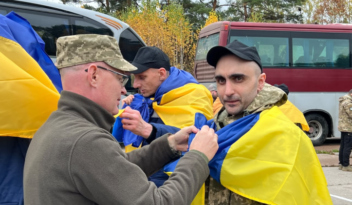 Upon his return from Russian captivity, the Ukrainian defender is draped in the national flag near the buses.