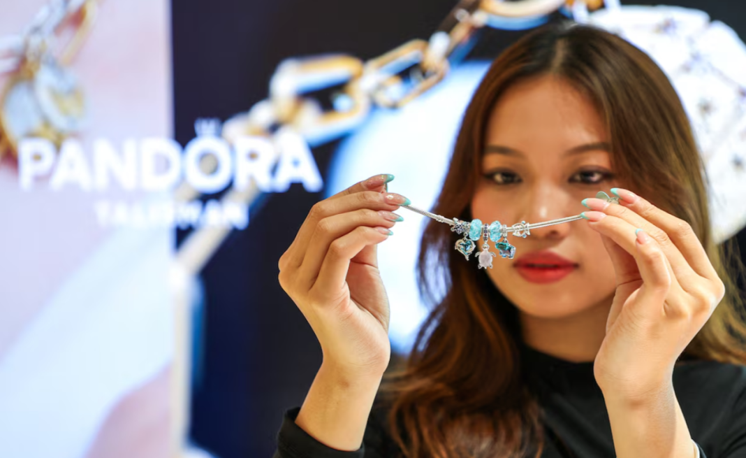 Pandora A woman is holding a silver Pandora bracelet with charms in front of her