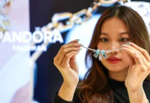 Жінка тримає перед собою сріблястий браслет Pandora із підвісками