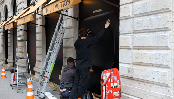 Staff are fitting protective panels to the windows of a Louis Vuitton boutique in France