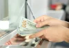 Долар наближається до 46 грн: скільки коштує в банках Жінка перераховує стодоларові банкноти біля касового вікна банку