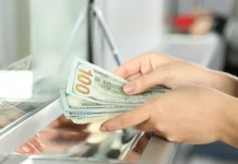 Жінка перераховує стодоларові банкноти біля касового вікна банку