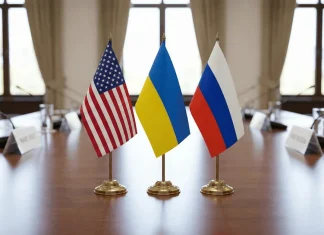 «Справа йде до завершення війни»: Ушаков анонсував можливий саміт Настільні прапори США, України та Росії на переговорному столі в дипломатичній залі.