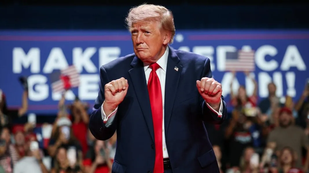 Президент США Дональд Трамп у темно-синьому костюмі та червоній краватці виступає перед прихильниками на політичному мітингу