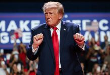 Президент США Дональд Трамп у темно-синьому костюмі та червоній краватці виступає перед прихильниками на політичному мітингу