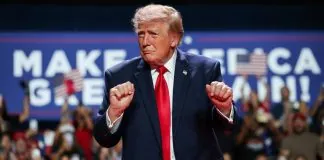 Президент США Дональд Трамп у темно-синьому костюмі та червоній краватці виступає перед прихильниками на політичному мітингу