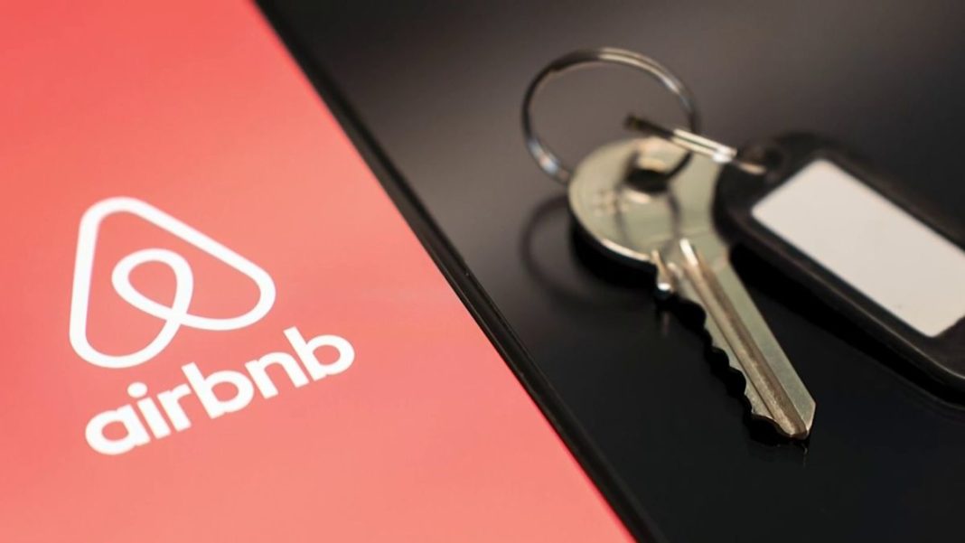 Логотип сервісу оренди житла Airbnb на екрані смартфона поруч із ключами від помешкання