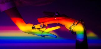 A person’s hands, illuminated by the colours of the rainbow, symbolising LGBTIQ+ rights and equality.