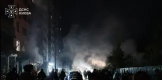 Люди стоять на нічній вулиці біля багатоповерхівки, звідки піднімається густий дим