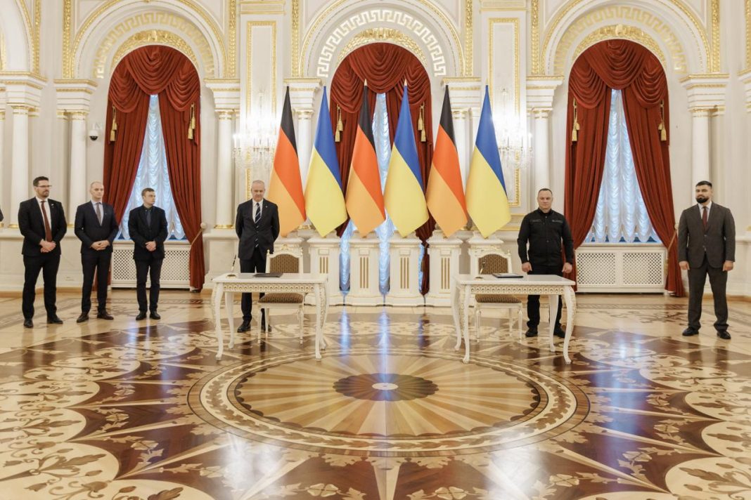 Декларація про співпрацю Посадовці стоять біля столів для підписання документів на тлі прапорів України та Німеччини