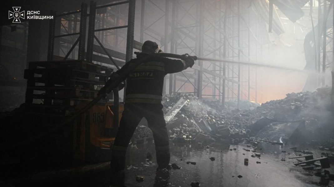 photo_2026-10-09_08-08-40 A State Emergency Service rescuer is putting out a fire amongst the ruins of warehouse structures following a Russian attack in the Bucha district of the Kyiv region.