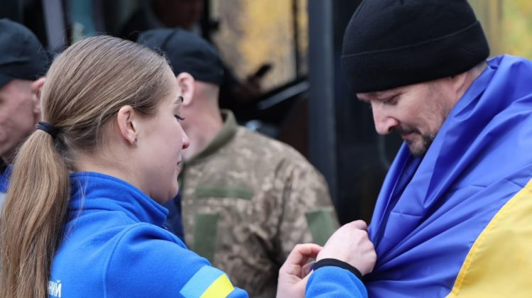 A Ukrainian soldier released from Russian captivity is draped in the national flag upon his return home.