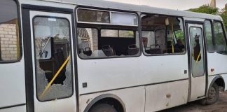 A white city bus with smashed windows and shards of glass on the seats inside the passenger compartment